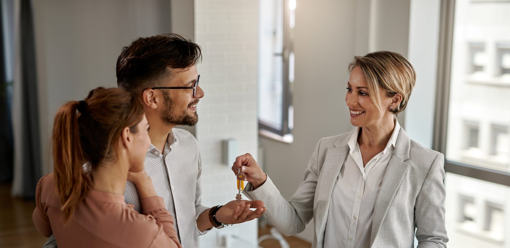 Happy real estate agent giving keys couple who is buying their new home copy