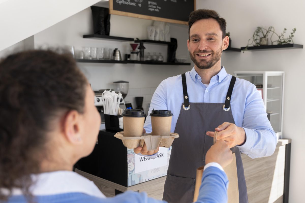 Man with apron offering packed takeaway food female customer