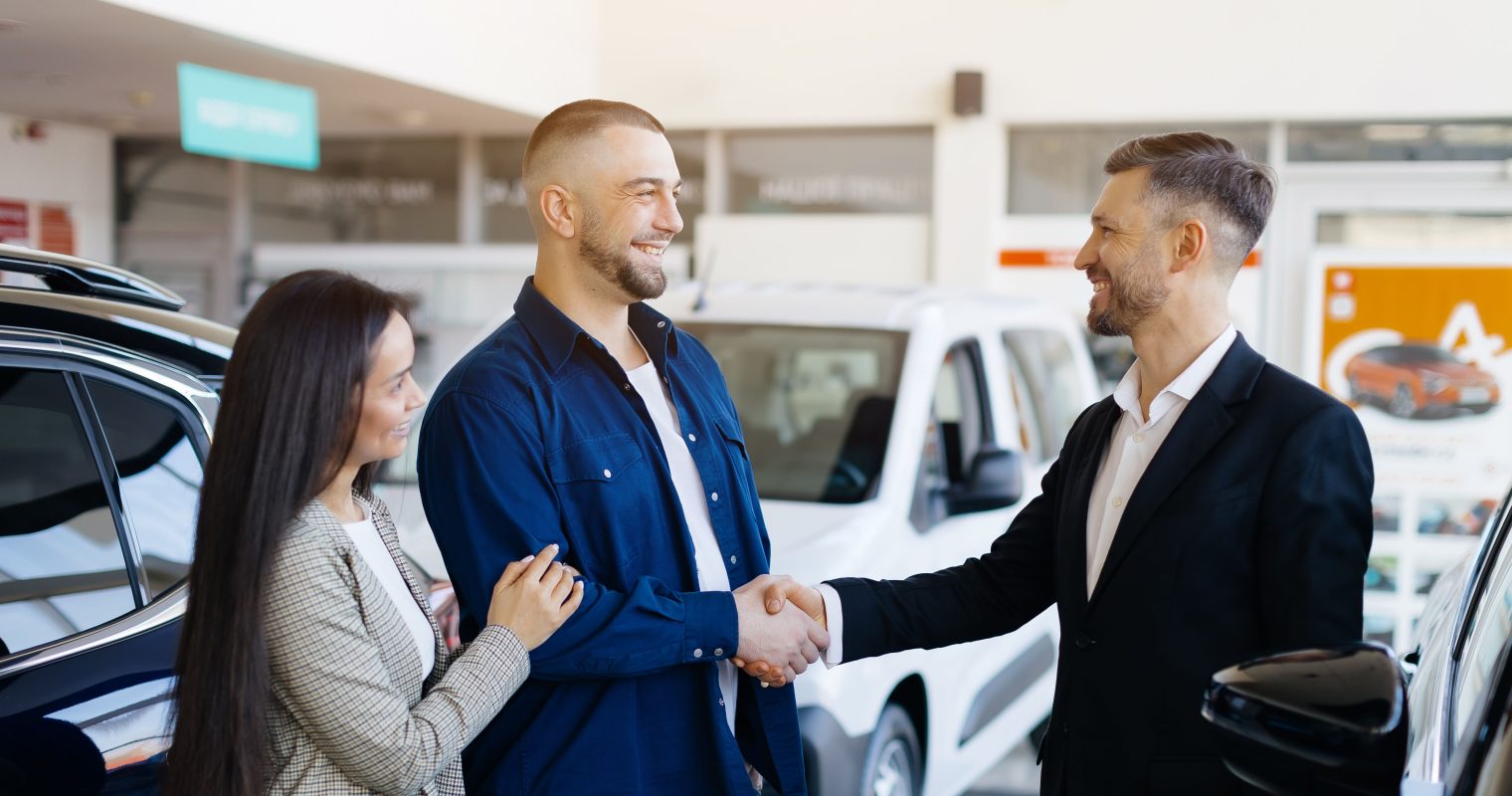 Sales manager helping young couple choose new car modern dealership center 1