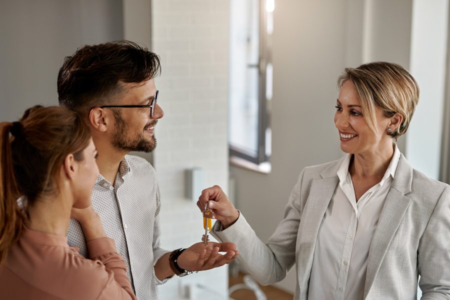 Happy real estate agent giving keys couple who is buying their new home copy