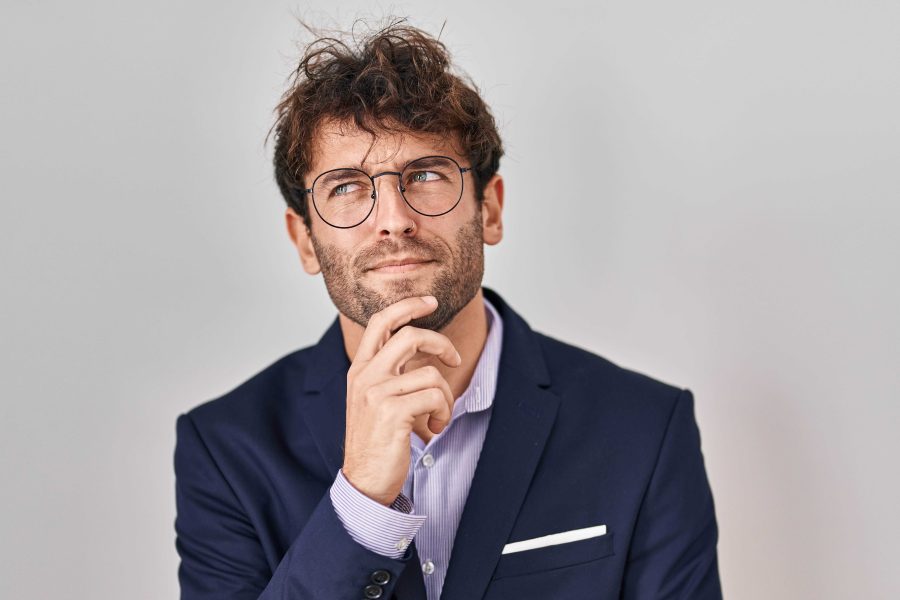 Hispanic business man wearing glasses with hand chin thinking about question pensive expression smiling with thoughtful face doubt concept copy