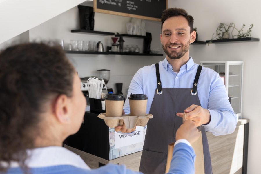 Man with apron offering packed takeaway food female customer