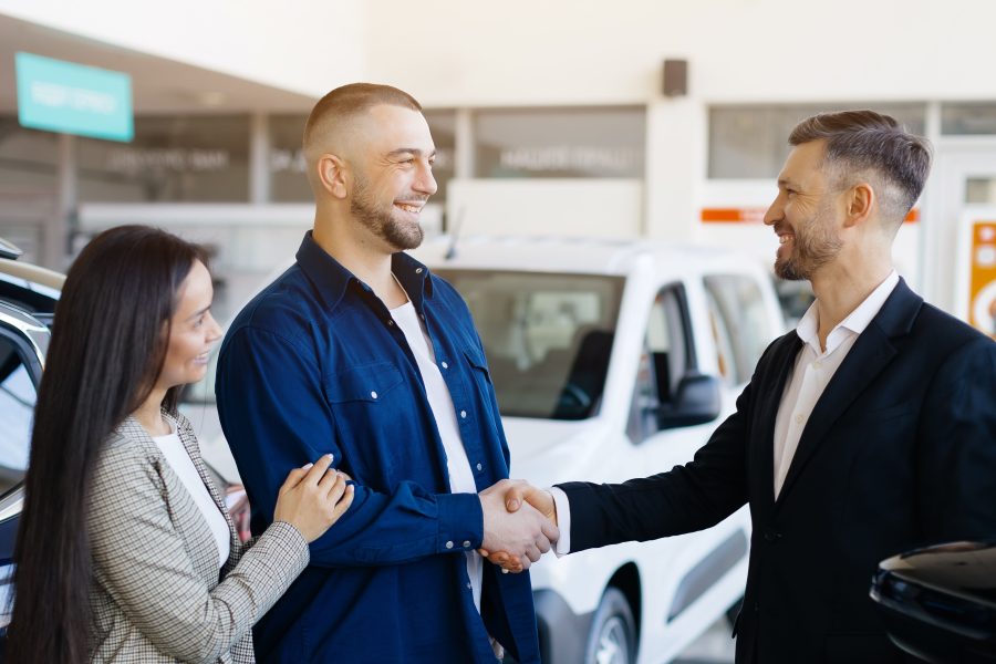 Sales manager helping young couple choose new car modern dealership center 1