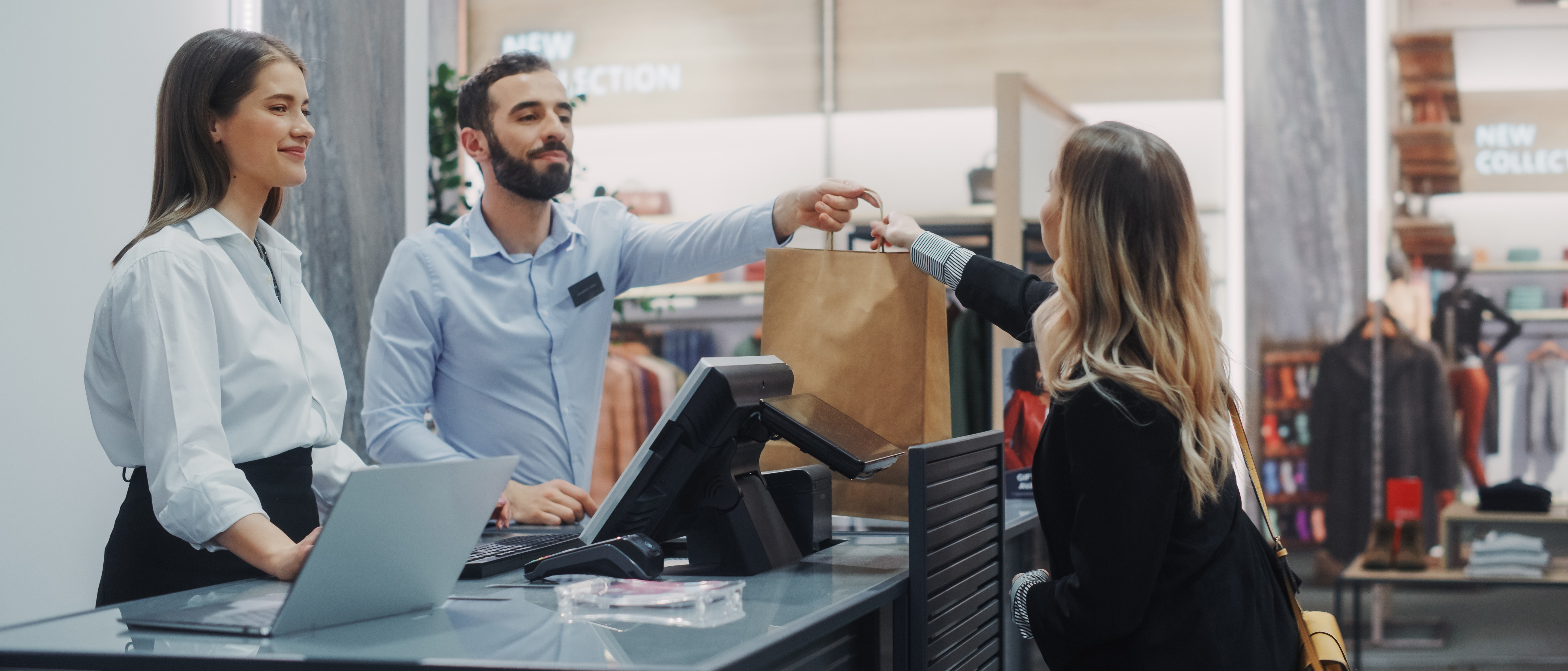 Clothing store checkout cashier counter beautiful young woman buys blouse from friendly retail sales assistant receiving bag with purchases trendy fashion shop with designer brands copy
